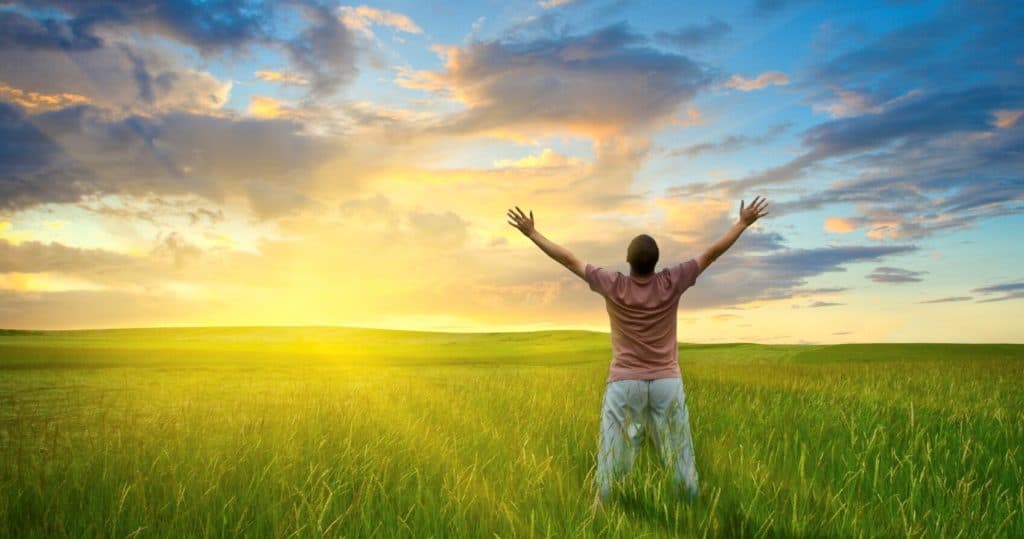 A man rejoicing in the view of a sunrise on a green field